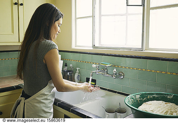 Young female washing hands in sink while working in kitchen at home
