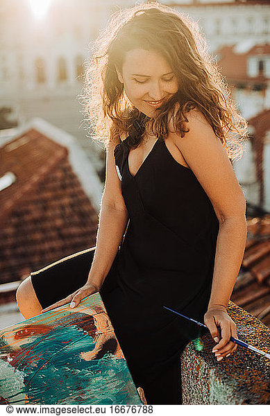 Young female woman sitting on roof with paint brush and painting