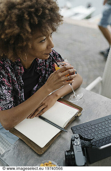 Young freelancer drinking and sitting with diary at table