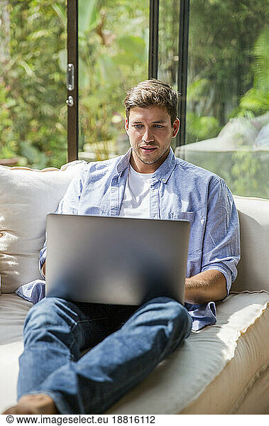 Young freelancer sitting on sofa and using laptop at home