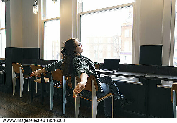 Young freelancer stretching arms in cafe