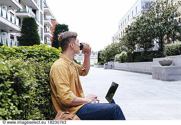 Young freelancer with laptop drinking coffee near plants