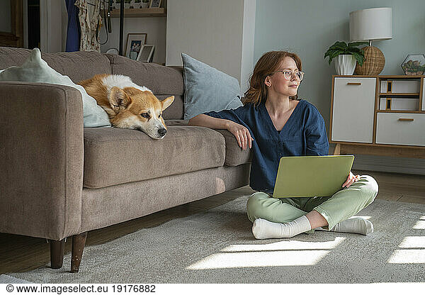 Young freelancer with laptop sitting by pet dog in living room