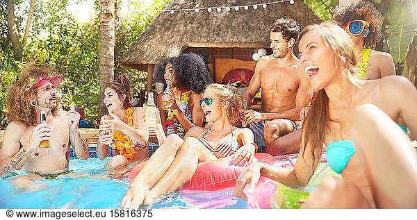 Young friends laughing  hanging out and drinking in sunny summer swimming pool
