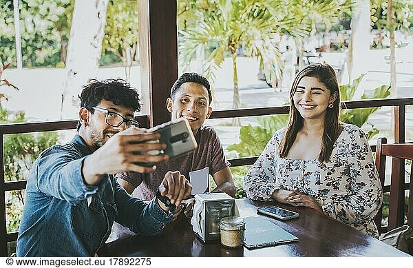 Young friends taking a selfie in a coffee shop. Three happy people in a coffee shop taking a selfie. Front view of teenage friends taking selfie and having fun in a cafe restaurant