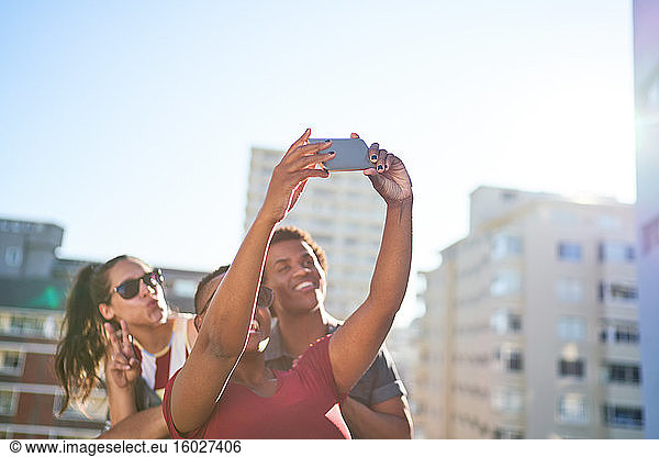 Young friends taking selfie with smart phone on sunny urban rooftop