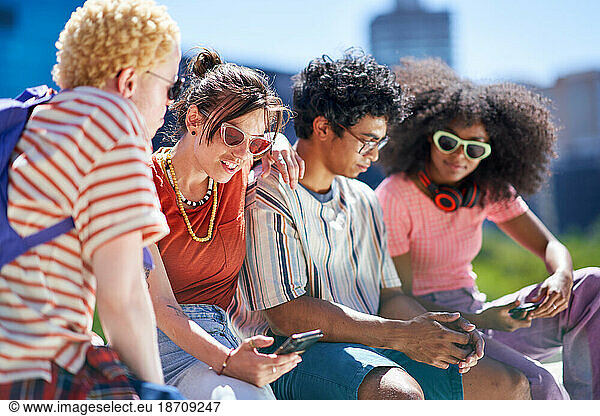 Young friends using smart phones in sunny city