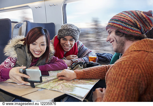 Young friends with map taking selfie with selfie stick on passenger train