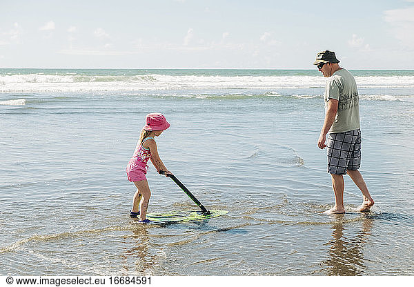 Young girl and her father playing on the beach with a skim board