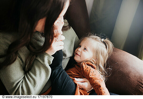 Young girl and her mother snuggle together on a chair in nursery
