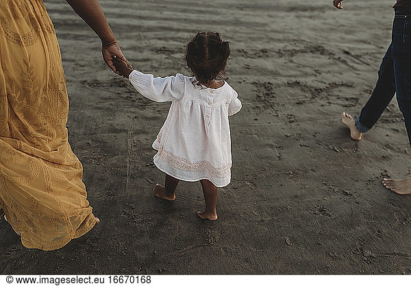 Young girl and mom walking away at beach holding hands