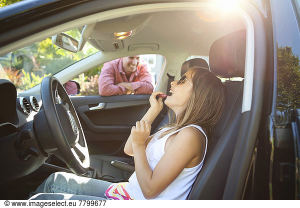 Young girl applying Lip Gloss  pretending to be old enough to drive as her smiling father watches on on a sunny summer evening in Portland  Oregon  USA