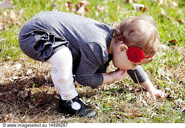Young Girl Bending Over Grass with Fingers in Mouth
