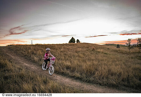 young girl bikes down a grassy hill at sunset