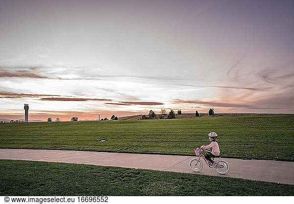 young girl bikes near a grassy hill at sunset