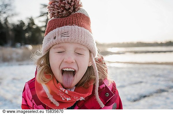 young girl catching snow with her tongue out whilst playing outside