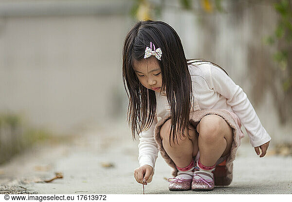 Young girl crouching to write on the ground; Hong Kong  China