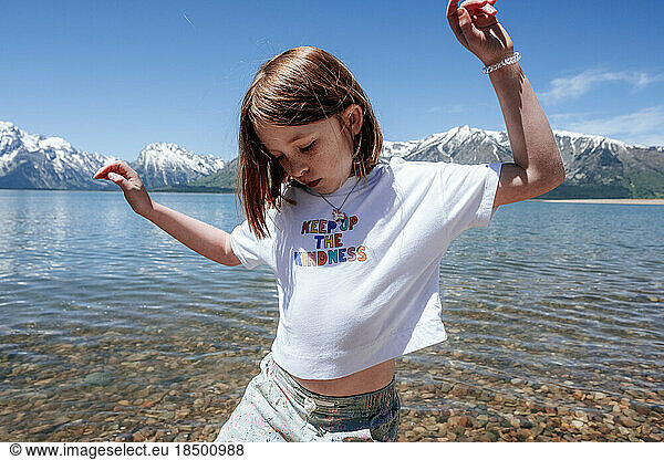 Young girl dancing on lake shore near snowy mountains
