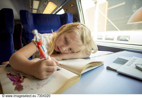 Young girl drawing pictures while sitting on train's seat