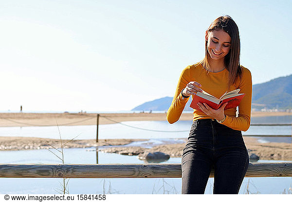 Young girl dressed in yellow reading a book on the beach.