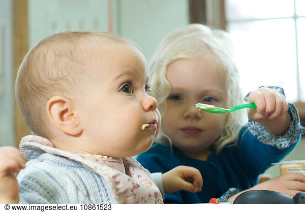 Young girl feeding baby sister with spoon