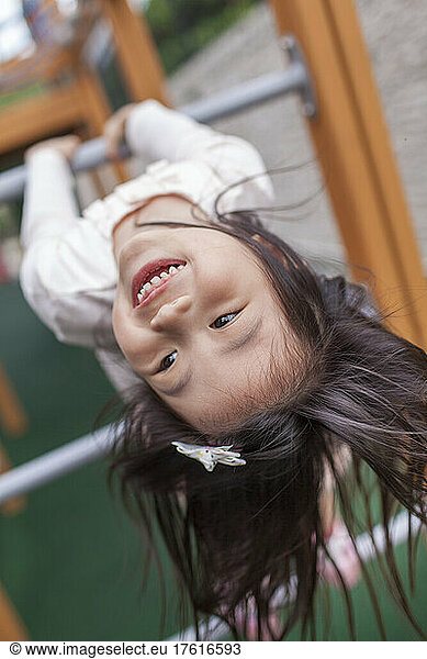 Young girl hanging upside down on climbing equipment at a playground; Hong Kong  China