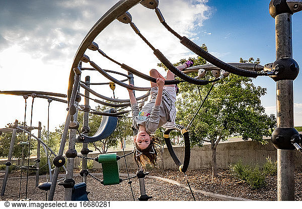young girl hangs upside down at playground