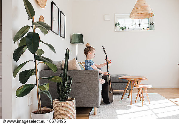 young girl holding a guitar  musical instrument whilst sat at home