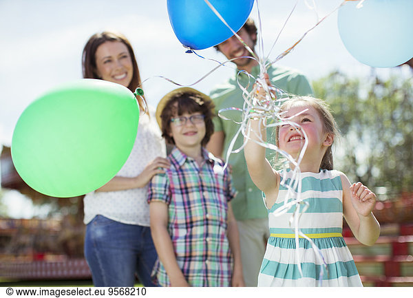 Young girl holding bunch of balloons  family standing behind her