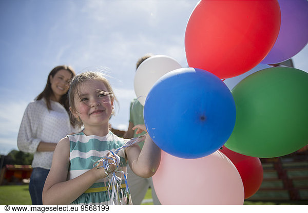Young girl holding bunch of colorful balloons at sunny day