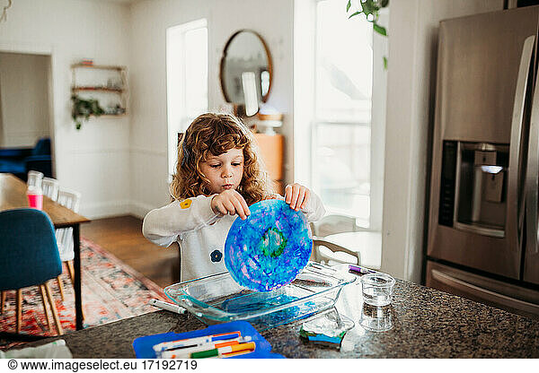 Young girl holding colorful art sitting at kitchen island