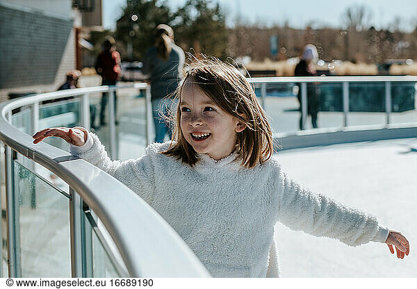 young girl holding on to rail while learning how to ice skate