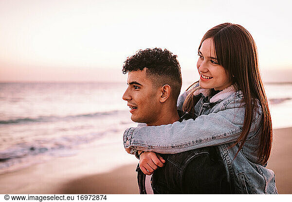 Young Girl Hugging Her Boyfriend's Back On The Beach At Sunset
