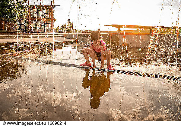 young girl in bathing suit squats over splash pad of squirting water