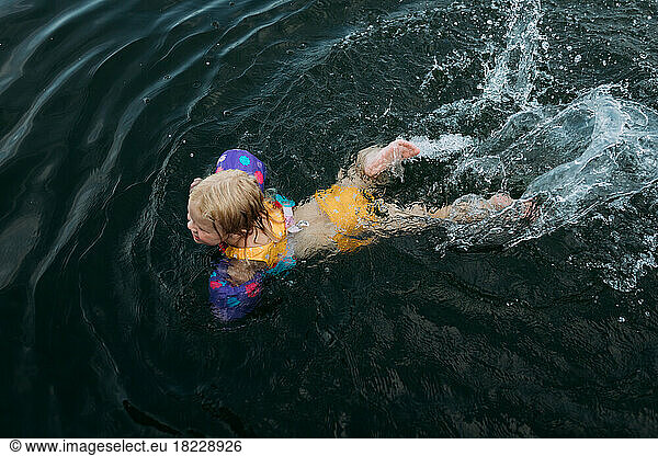 Young girl in colorful swimwear swimming in lake