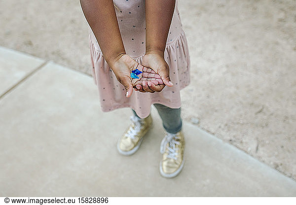 Young girl in pink dress with yellow shoes holding blue flower petals