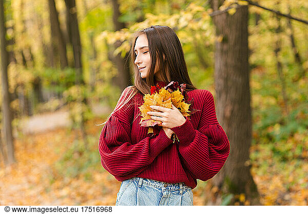 Young girl in red jumper holding maple leaves in forest