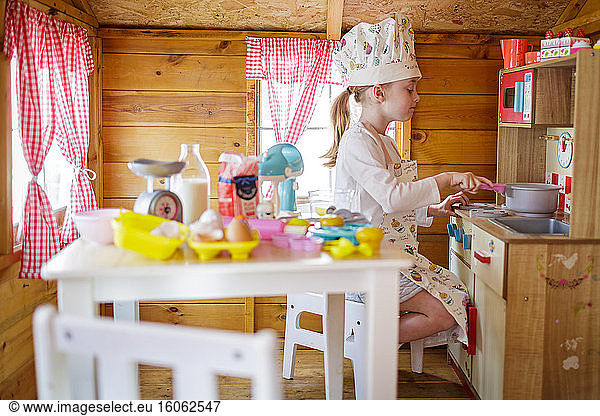 Young girl in wendy house pretending to cook in kitchen