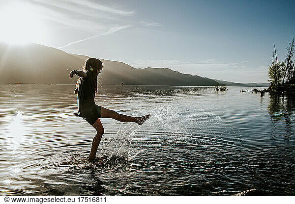 Young girl kicking and splashing in water at a lake