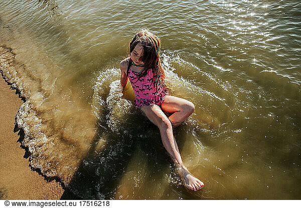 Young girl laying on lake shore in water