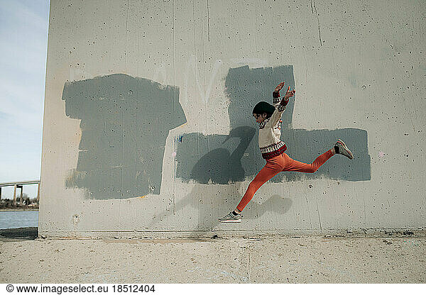 Young Girl Leaping cement wall with painting under a bridge