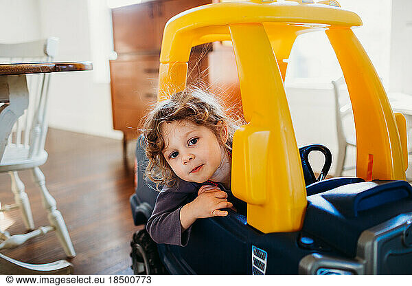 Young girl looking at camera sitting in toy car inside dining room
