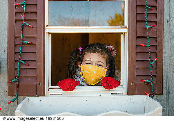 Young girl looking through window with face mask Christmas lights