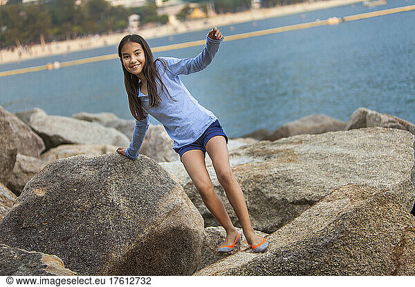 Young girl looks at the camera while climbing on large rocks at Repulse Bay; Hong Kong  China