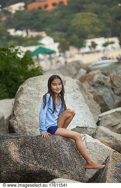 Young girl looks at the camera while sitting on rocks at Repulse Bay; Hong Kong  China