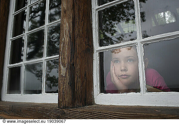 Young girl looks out window of cabin at Kezar Lake  Maine