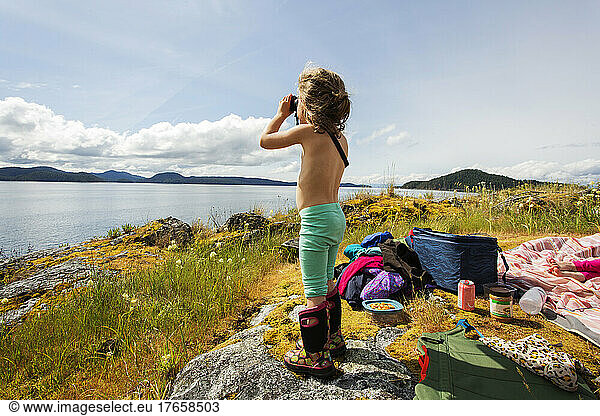 Young girl looks through binoculars from rocky island on bay