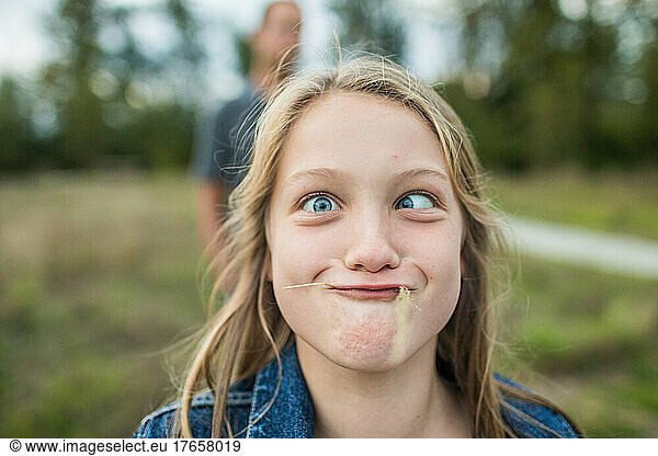 Young girl makes sill face  crazy eyes  grass in mouth.