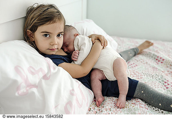 Young girl on bed with pillows cuddling newborn baby