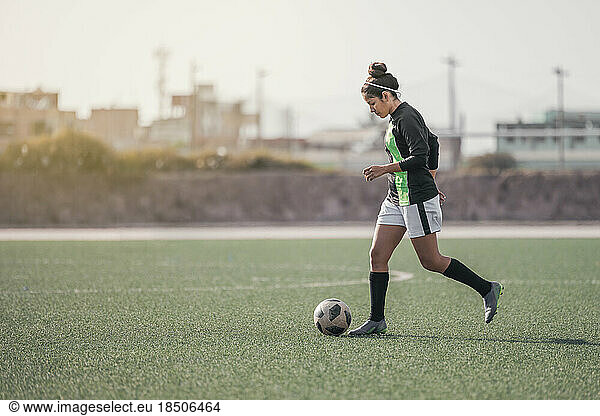 Young girl on the grass kicking a soccer ball and smiling